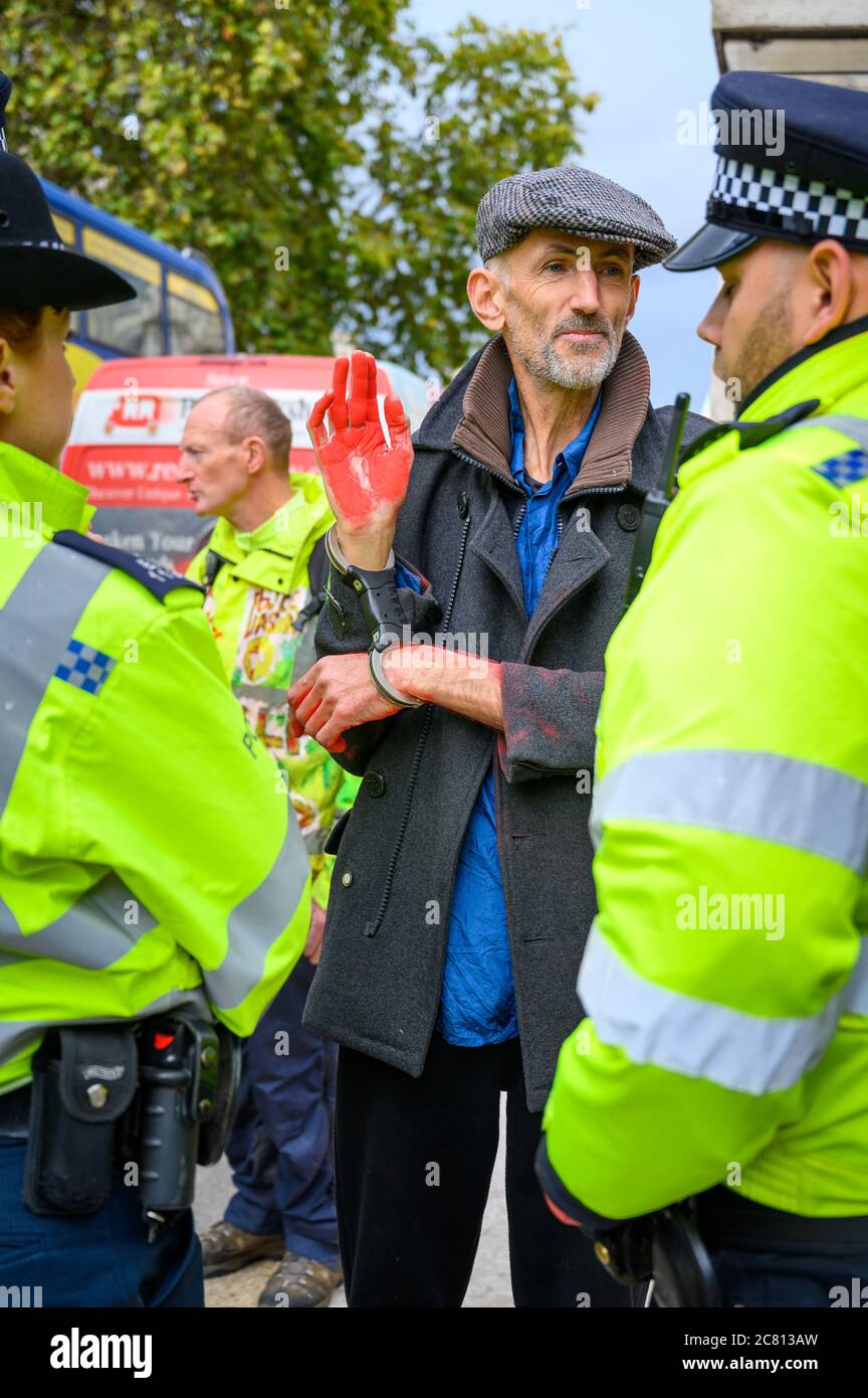 LONDON - OCTOBER 18, 2019: Vertical shot of Handcuffed male Extinction Rebellion protester with red painted hand surrounded by Police Officers Stock Photo