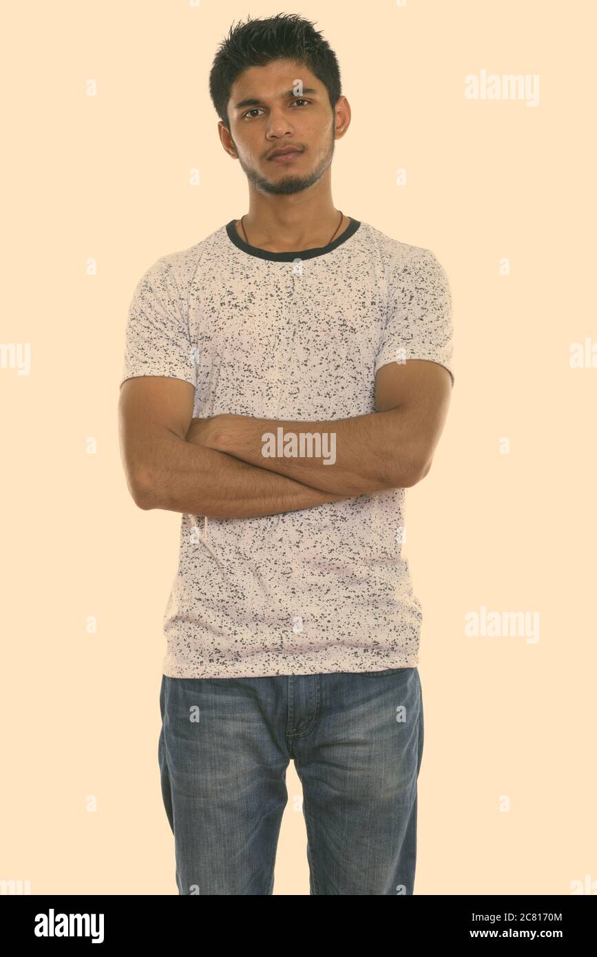 Studio shot of young handsome Indian man standing with arms crossed ...