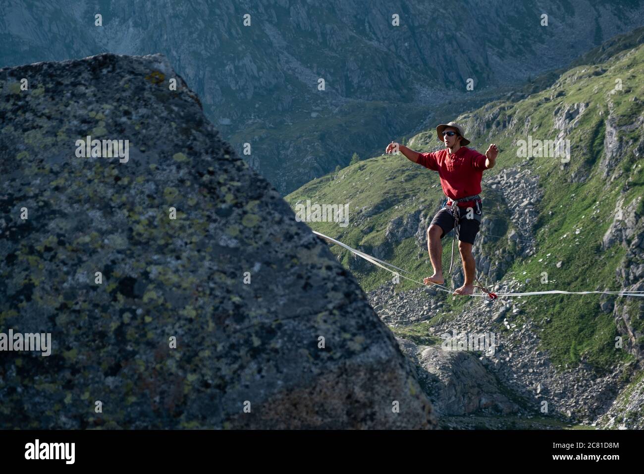 Lago Nero, Pinzolo, Italy - 2020 july 18th: young boy with red hoodie and hat practising slackline on a rope hanging between two peaks, great height a Stock Photo