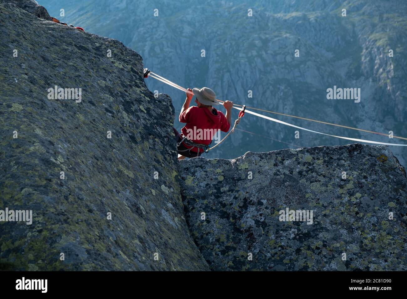 Lago Nero, Pinzolo, Italy - 2020 july 18th: young boy with red hoodie and hat practising slackline on a rope hanging between two peaks, great height a Stock Photo