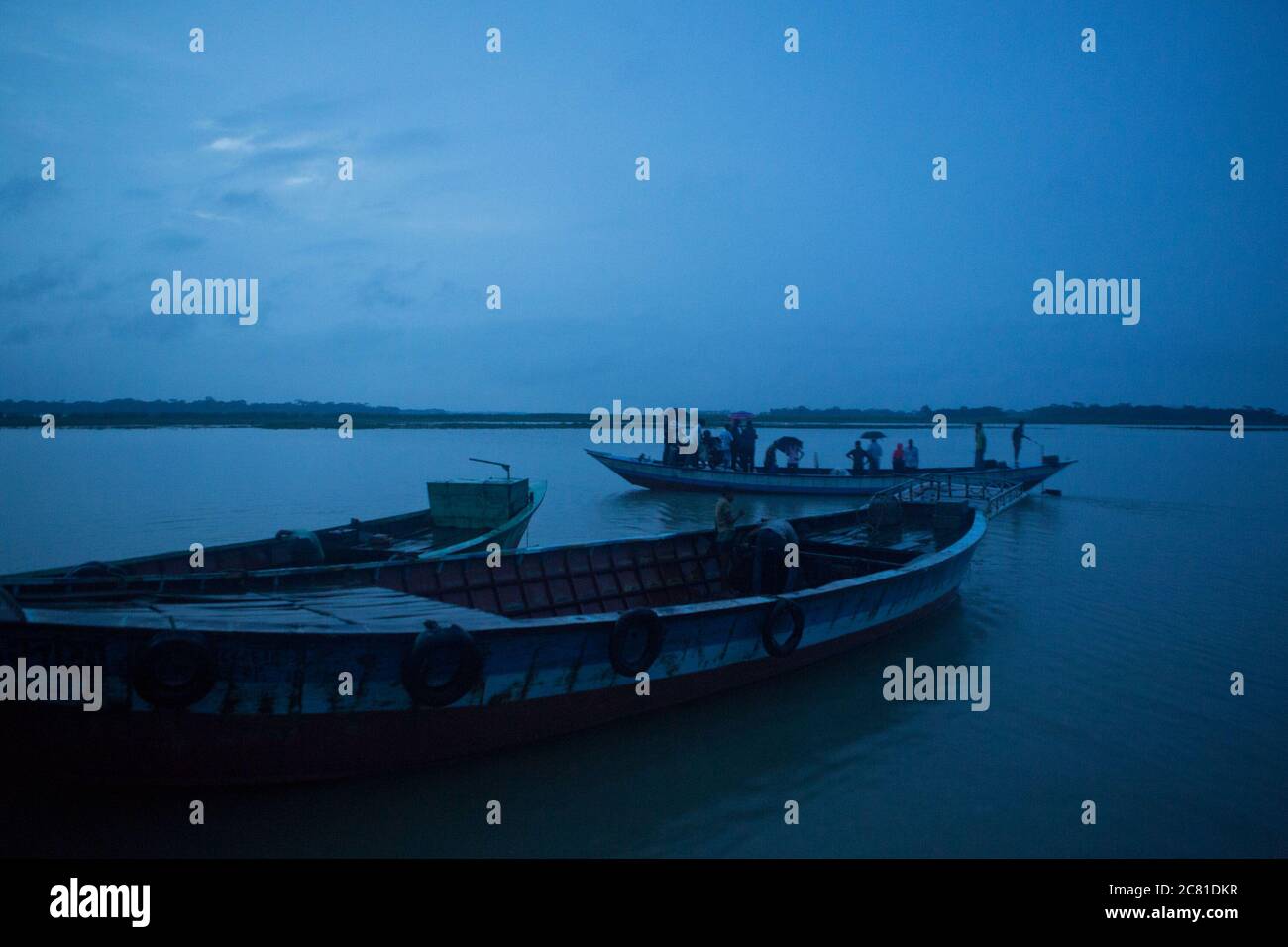 Blue evening light covers the boats and waters of the river Kirtonkhal, near Barisal, Bangladesh. These country boats carry passengers while others are idle and float on the water of the river. Stock Photo