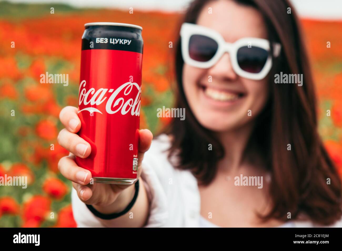 Lviv, Ukraine - Jun 11, 2020: Woman drinking coca cola standing at the field of poppy flowers. hot summer day Stock Photo