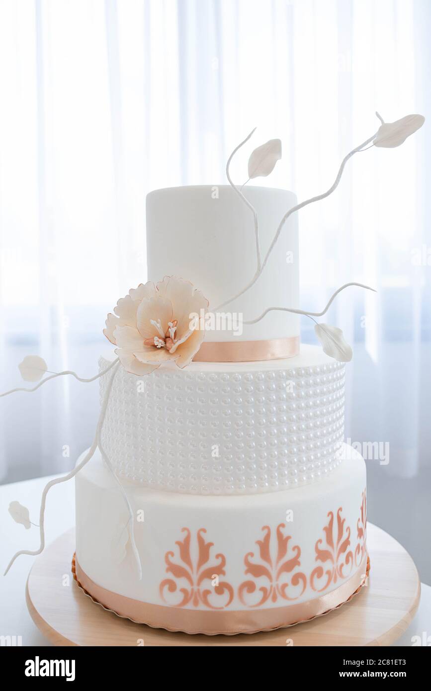 Elegant three tier wedding cake, covered in royal icing with beautiful peach color accents, edible flowers and details, part of a baking workshop Stock Photo