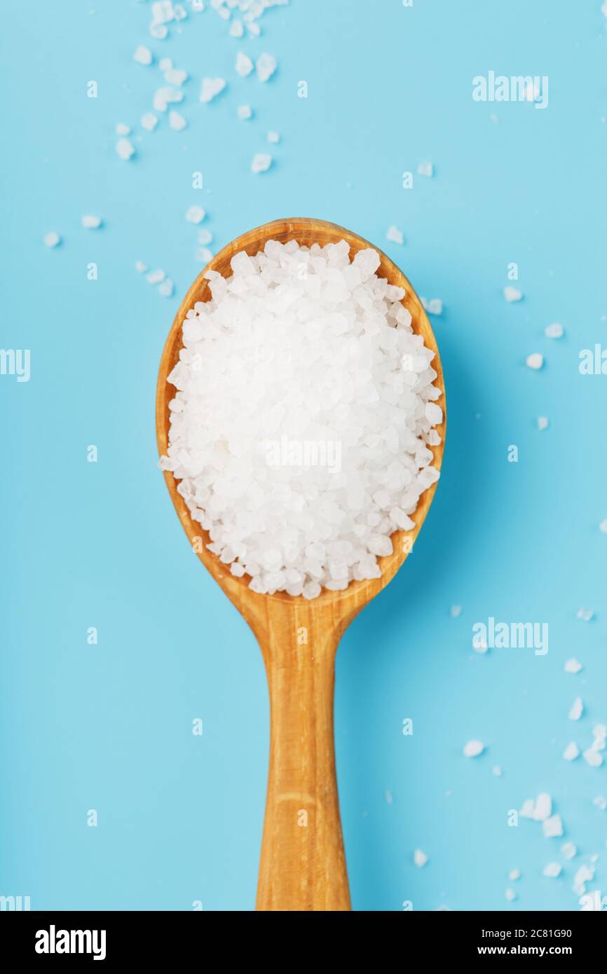 Large sea salt crystals in a wooden spoon with greens on a blue background. Stock Photo