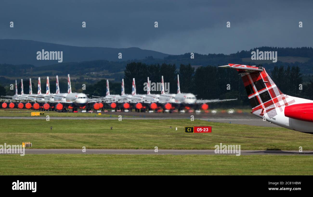 Glasgow, Scotland, UK. 20th July, 2020. Pictured: Loganair Embraer ERJ145 plane seen at Glasgow Airport with a large group of grounded British Airways (BA) airbus aircraft in the background. Loganair had taken over some of Flybe's slots after the collapse of Flybe, then the coronavirus lockdown hit in March, and since then Loganair have been increasing services but these are turbulent times for all airlines and the global aviation industry. Credit: Colin Fisher/Alamy Live News Stock Photo