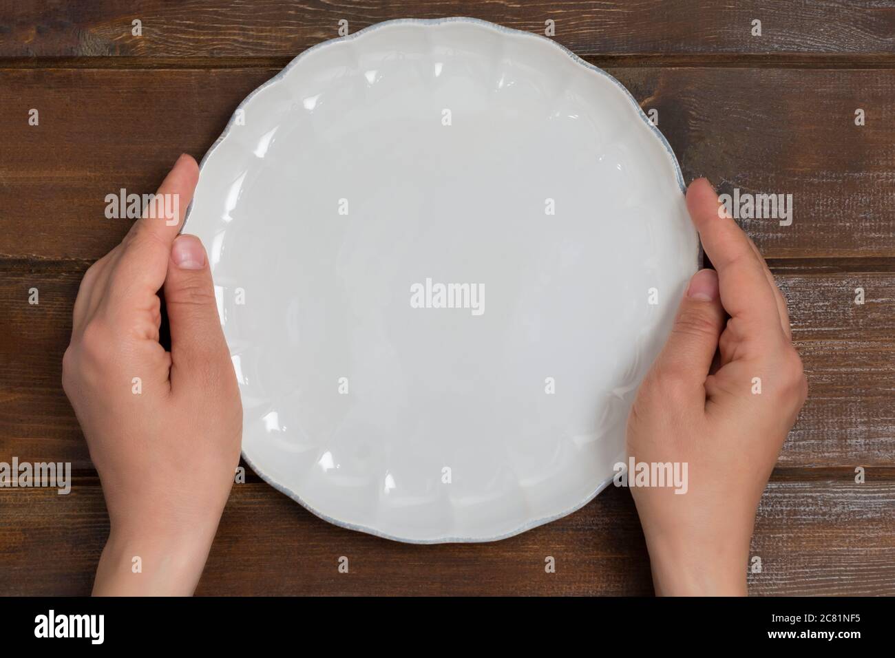 Top view of woman hands holding white empty plate on wooden background with copy space Stock Photo