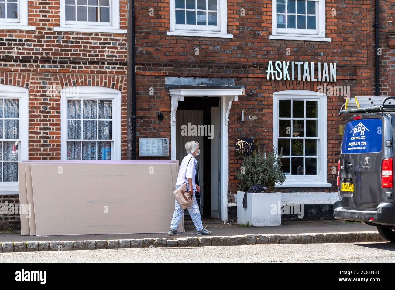 20th July 2020. Old Amersham, Buckinghamshire, UK. The ASK Italian and Zizzi restaurant chain announced 2 days ago they are permanently closing 75 restaurants due to loss of income during the coronavirus covid-19 pandemic lockdown. A woman wearing a face mask walks past an ASK Italian restaurant while it is about to be boarded up. Stock Photo