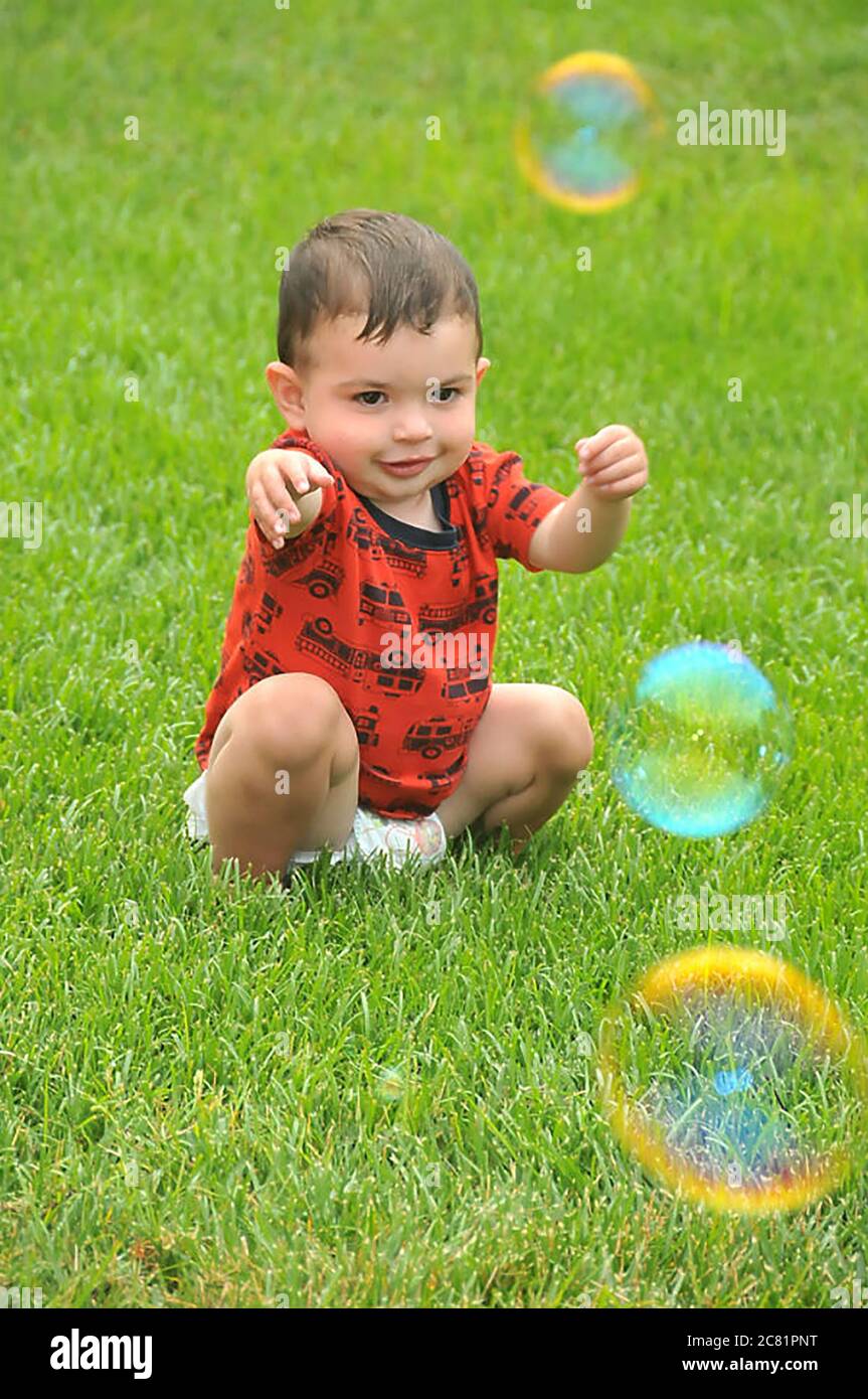 A male toddler sitting on the lawn fascinated by bubbles Stock Photo
