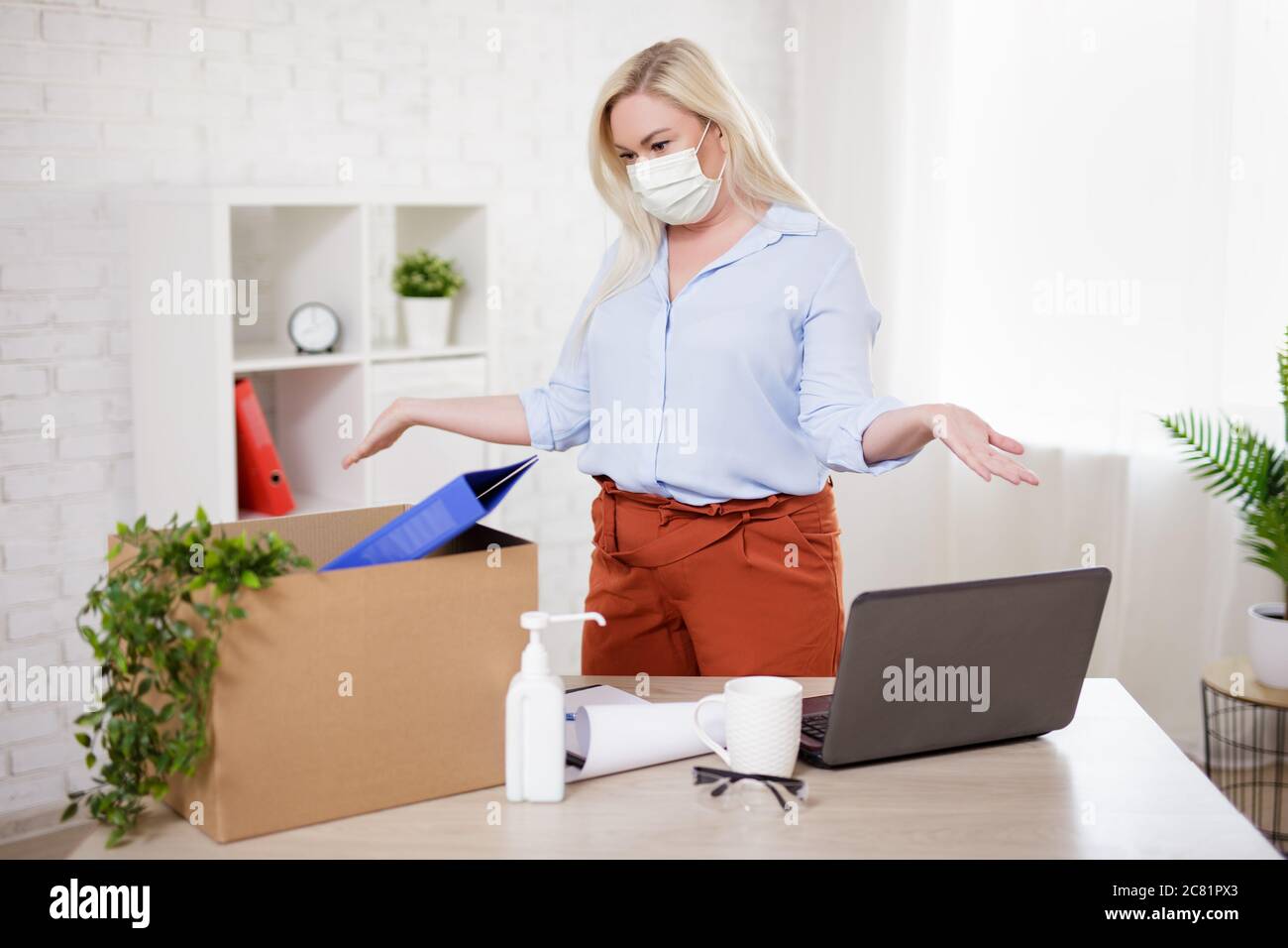 business, financial crisis, health care, safety and corona virus pandemic concept - woman in mask packing belongings after getting fired from her work Stock Photo