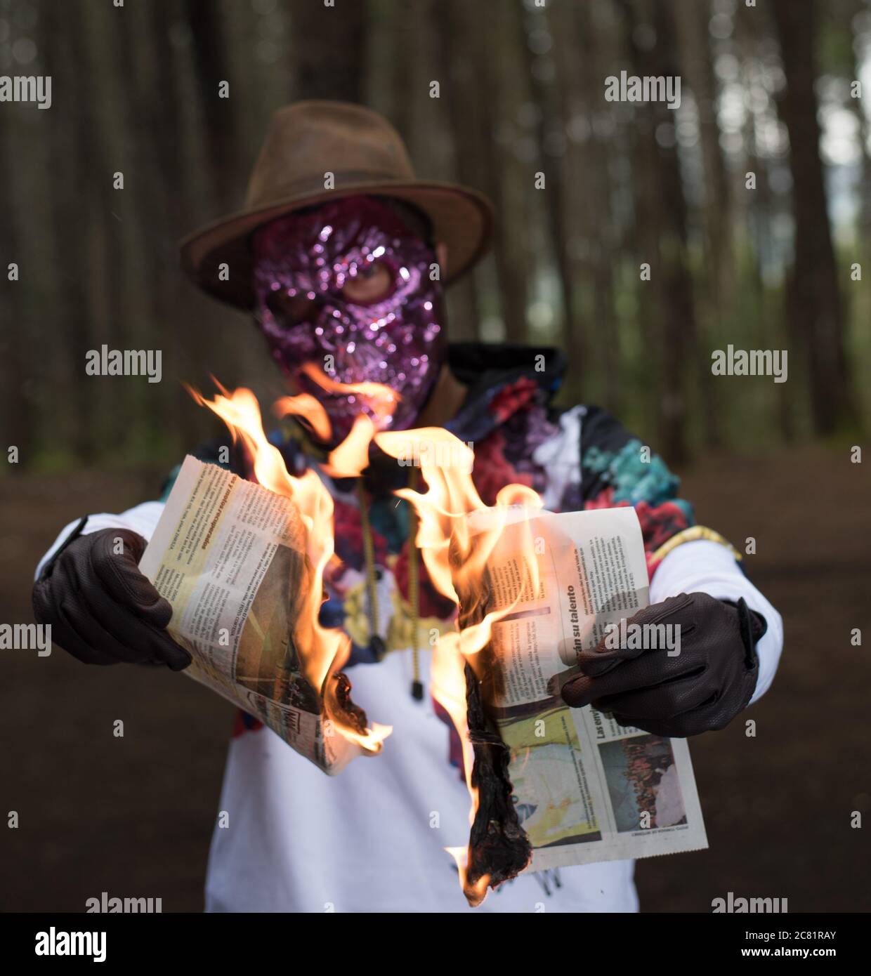 Unknown person wearing a scary face mask burning the newspaper in a forest - crime concept Stock Photo