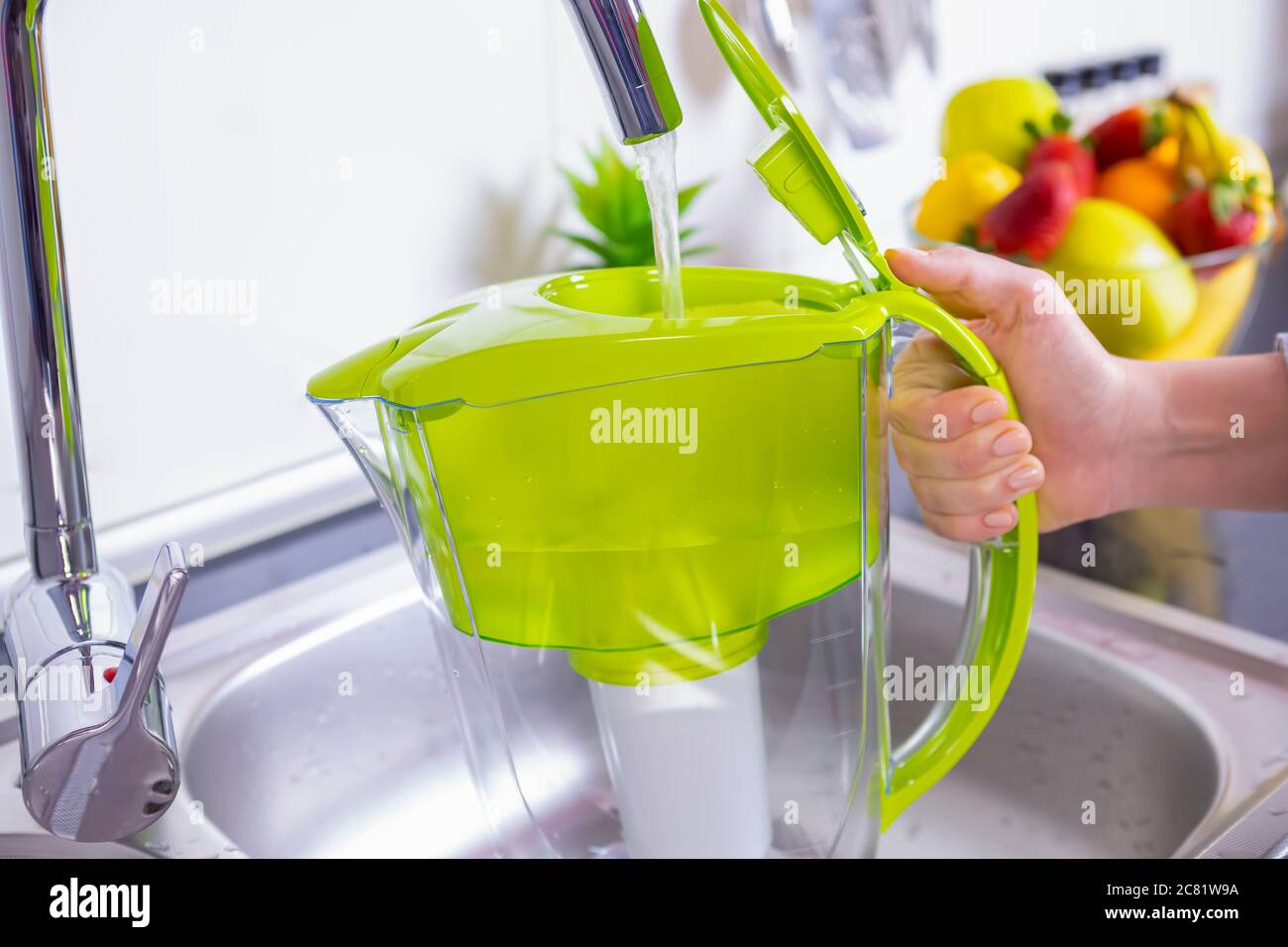 Woman filling water filter jug in the kitchen. Purification and softening of drinking tap water. Closeup Stock Photo