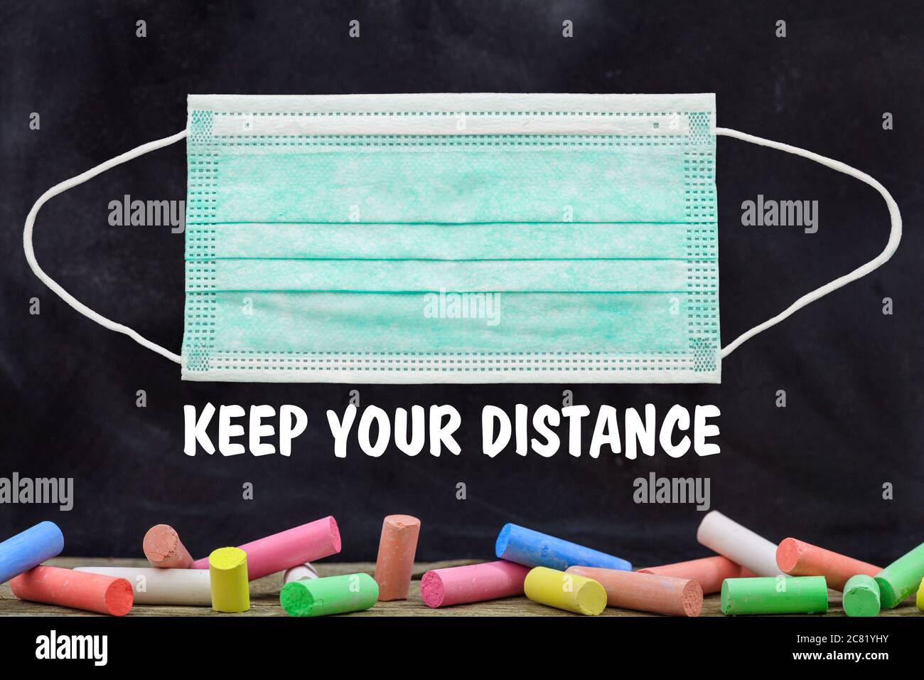 KEEP YOUR DISTANCE text and blank protective mask against blackboard with colorful chalks background, Coronavirus spread in school prevention measure, Stock Photo