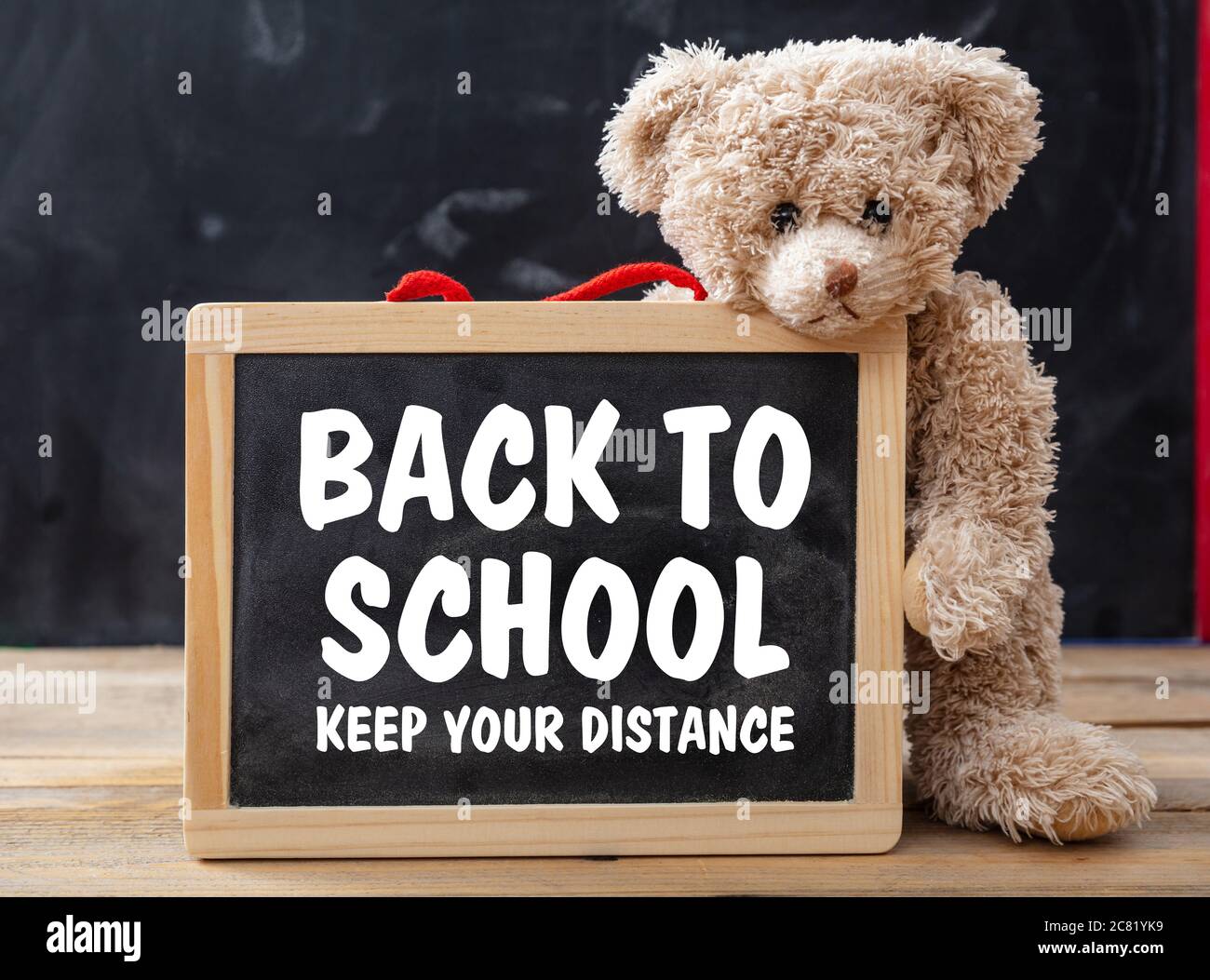 BACK TO SCHOOL KEEP YOUR DISTANCE text message, teddy bear holding a blackboard, classroom background, Coronavirus spread in school prevention measure Stock Photo