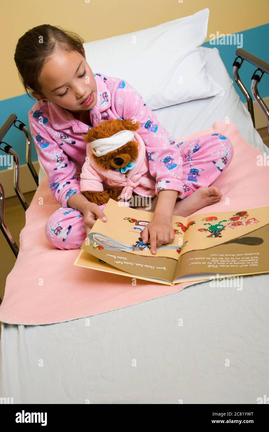 Young girl reading story in hospital bed; Alberta, Canada Stock Photo