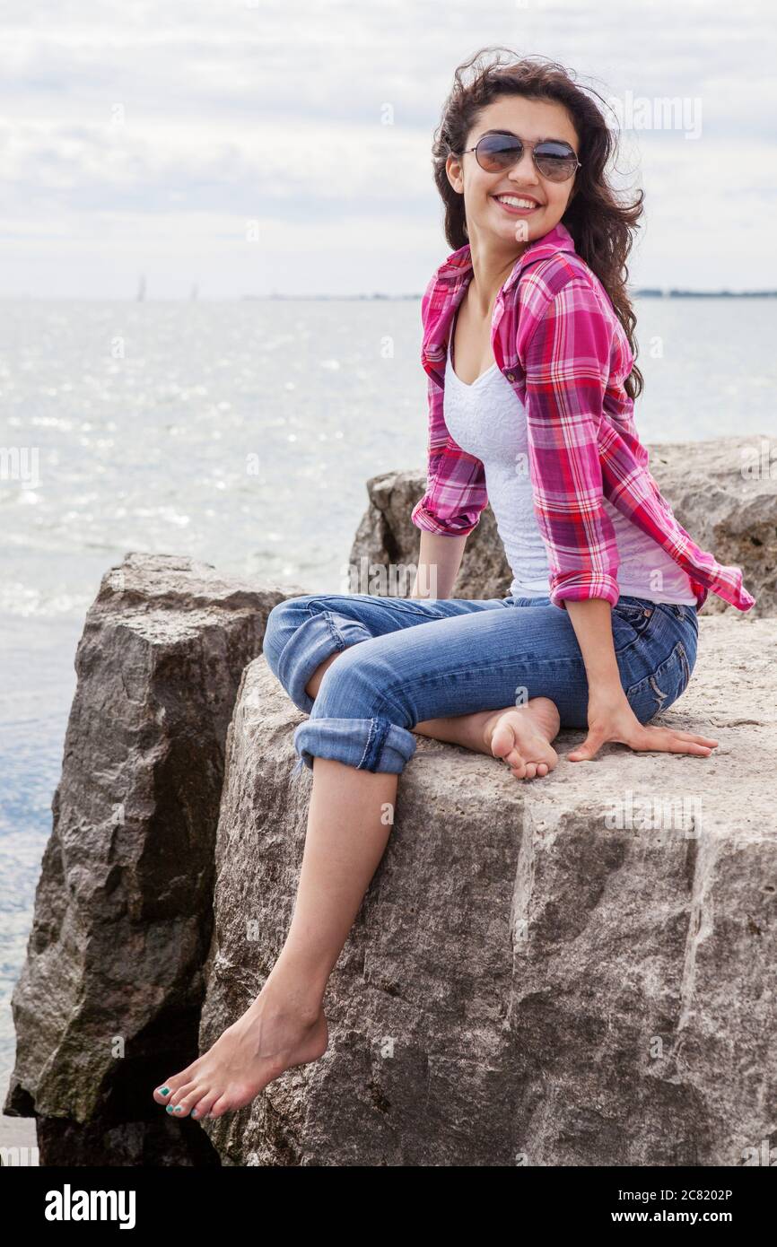 Teenage girl sitting on rocks looking out at the lake, Woodbine Beach; Toronto, Ontario, Canada Stock Photo