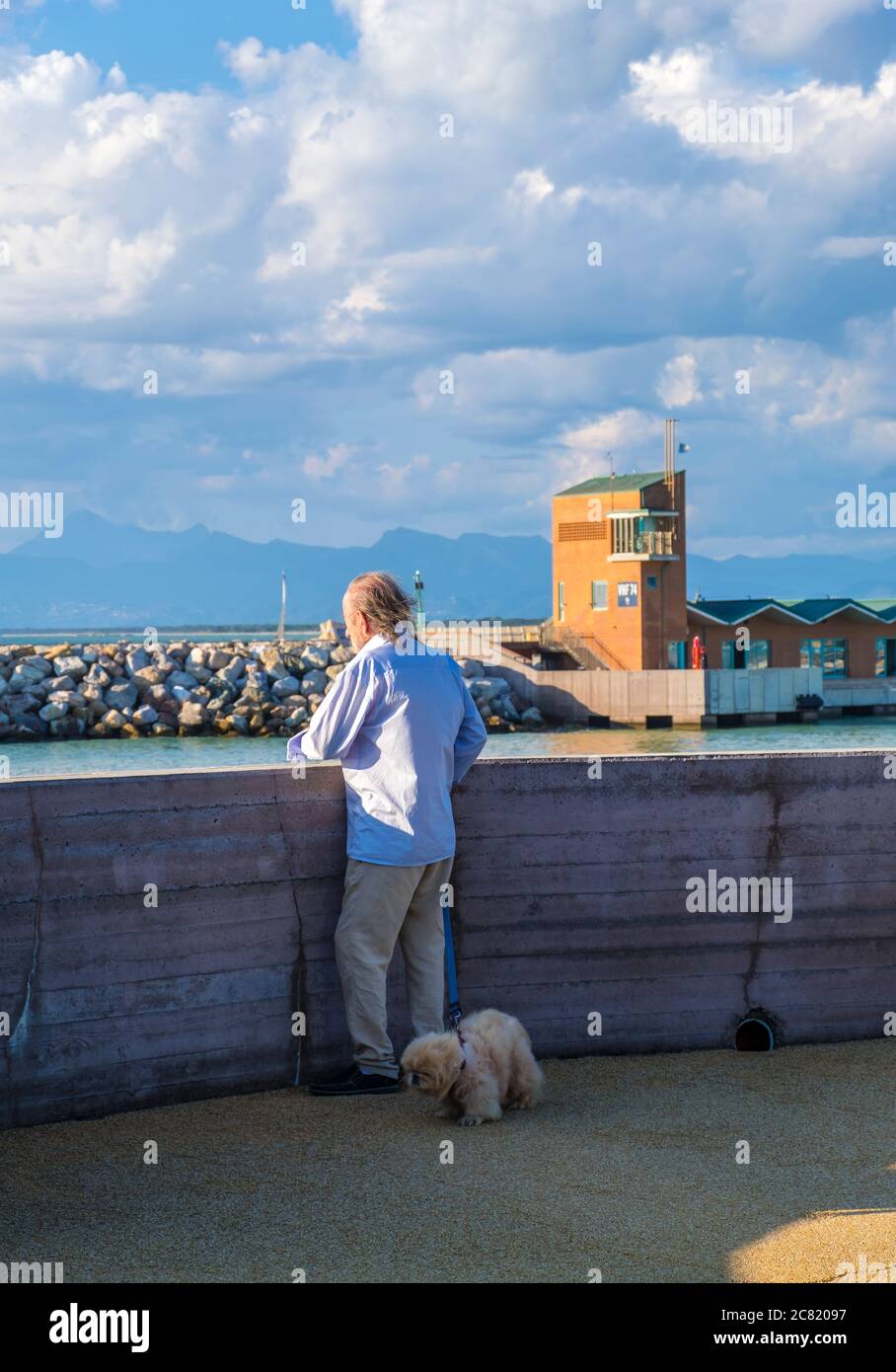 Marina di Pisa, Italy - August 14, 2019: Elderly man with a dog admiring the beautiful view in the Port of Pisa in Marina di Pisa, Tuscany, Italy Stock Photo