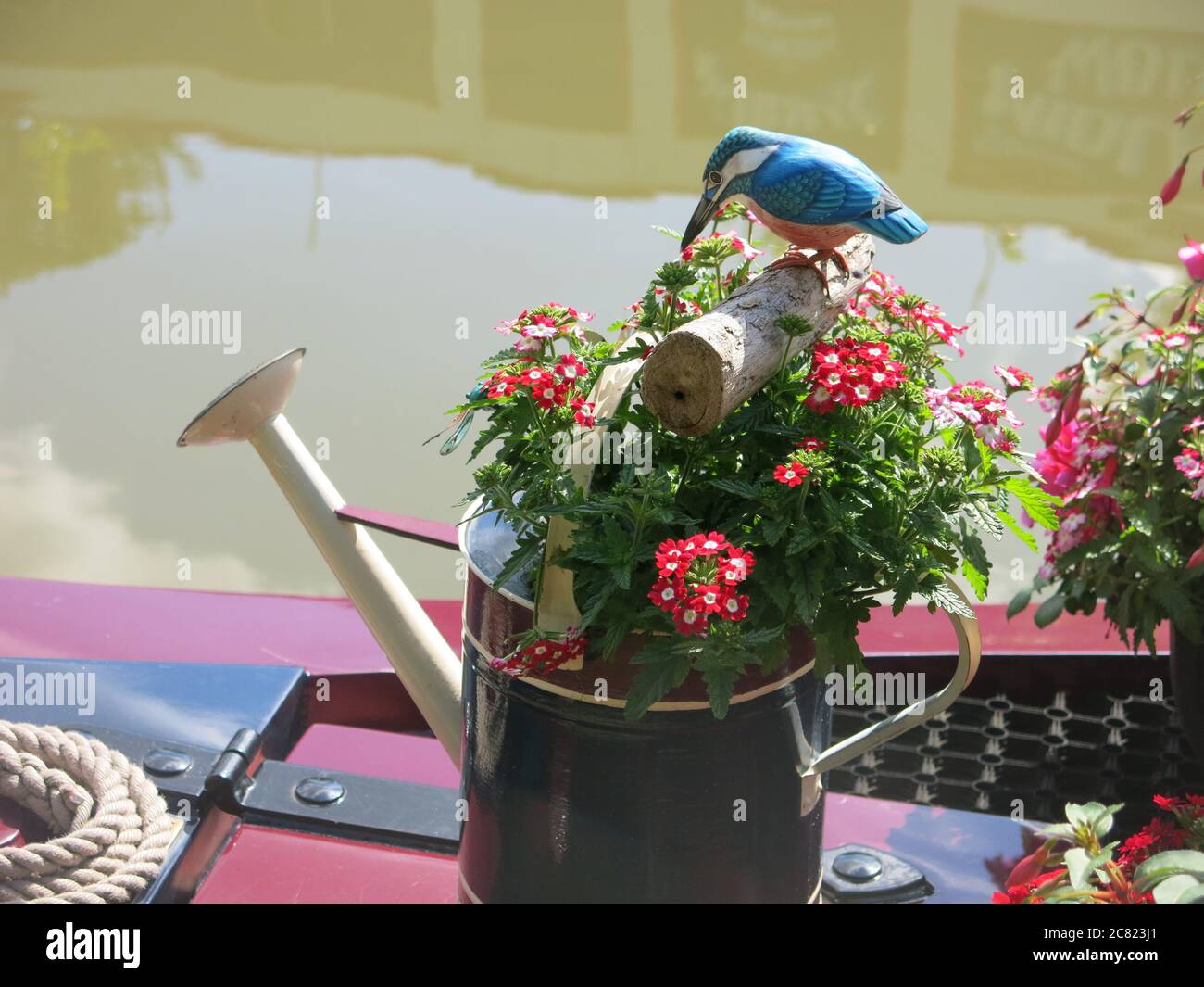 A decorated watering can painted in canal folk art style, filled with summer planting and a model bird on a log. Stock Photo