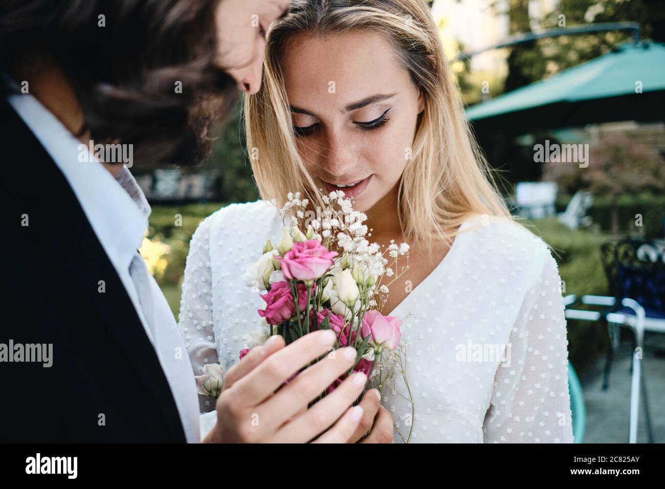 Close up romantic groom and gorgeous bride sensually holding bouquet of flowers outdoor Stock Photo