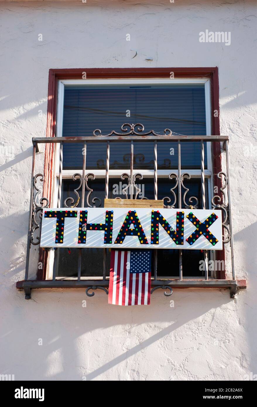 Hand made THANX or THANKS sign hanging from balcony window of neighborhood home. Included is the American flag and lights for night viewing. Stock Photo
