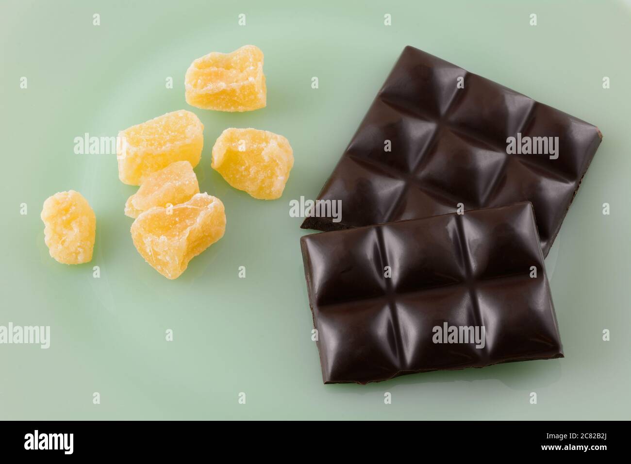 Closeup of dark chocolate candy bar pieces and crystallized ginger on green plate Stock Photo