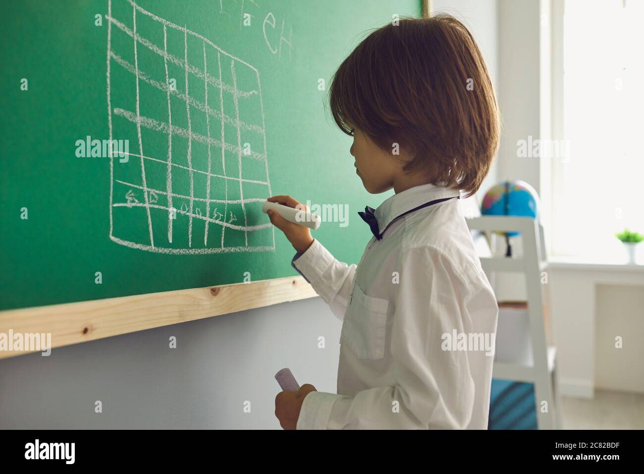 Chess lesson for children. Boy draws a chessboard on the green board in the classroom. Stock Photo