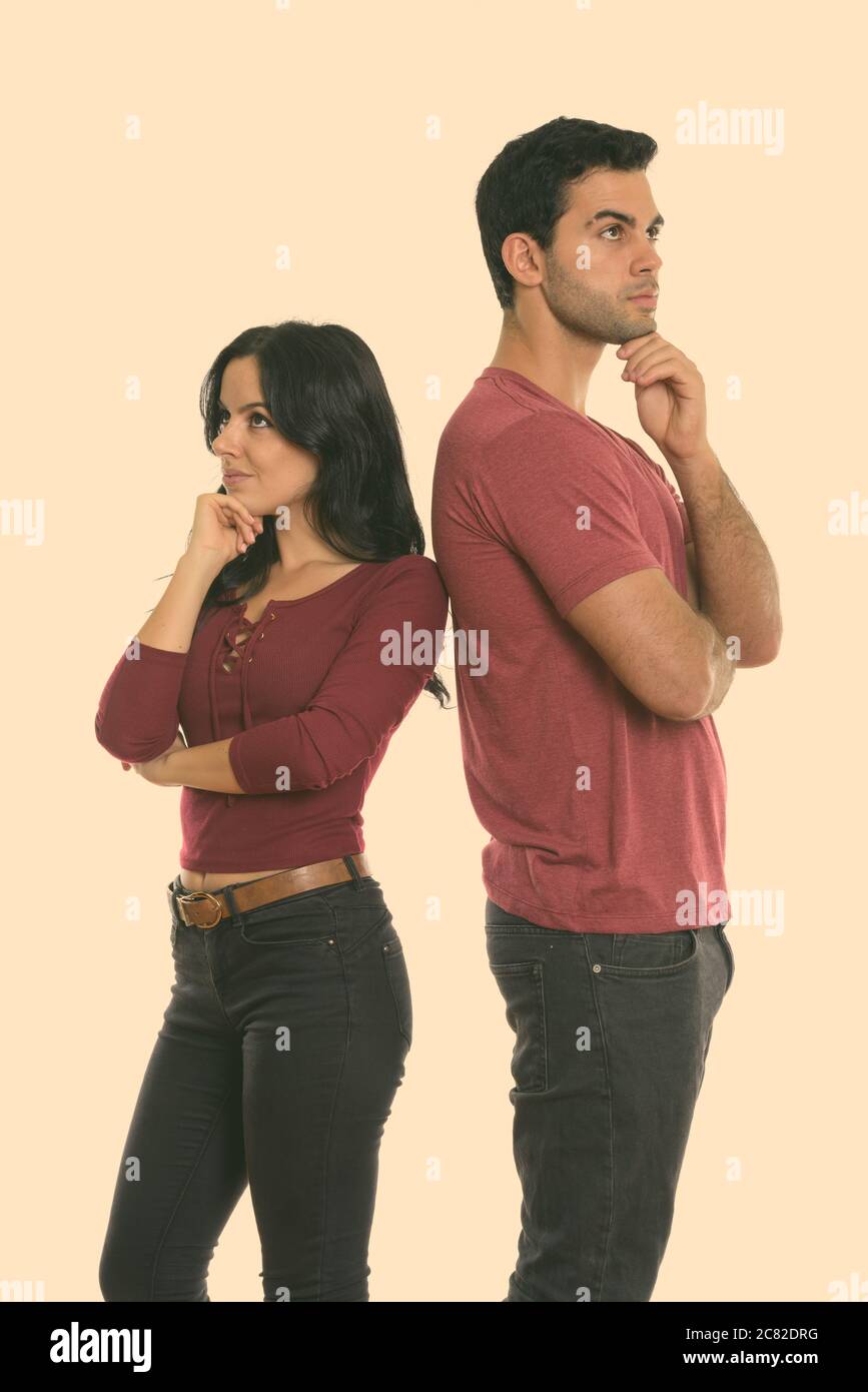 Studio shot of young couple standing while thinking and looking up together with back to back Stock Photo