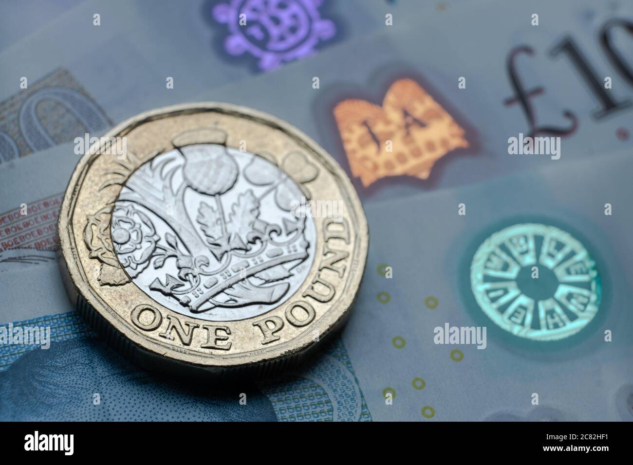 British one Pound coin place on top of new polymer banknotes with visible pound symbol and hologram, Stock Photo