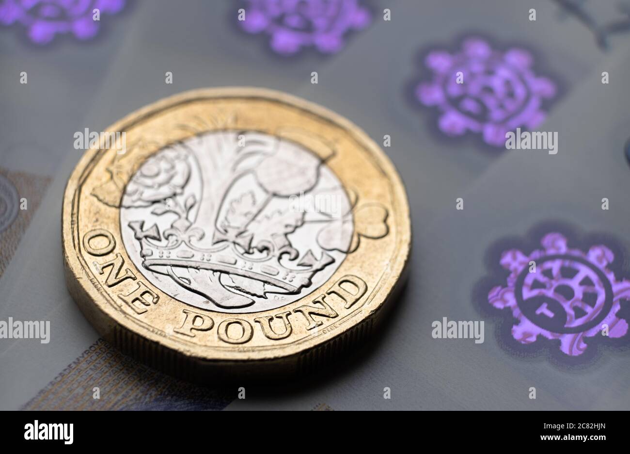 British one Pound coin place on top of new polymer banknotes with visible pound symbol and hologram, Stock Photo