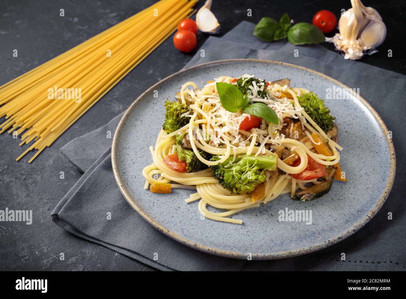 Spaghetti pasta with vegetables and parmesan, vegetarian meal and ingredients on a grey-blue plate and a dark rustic background, selected focus, narro Stock Photo