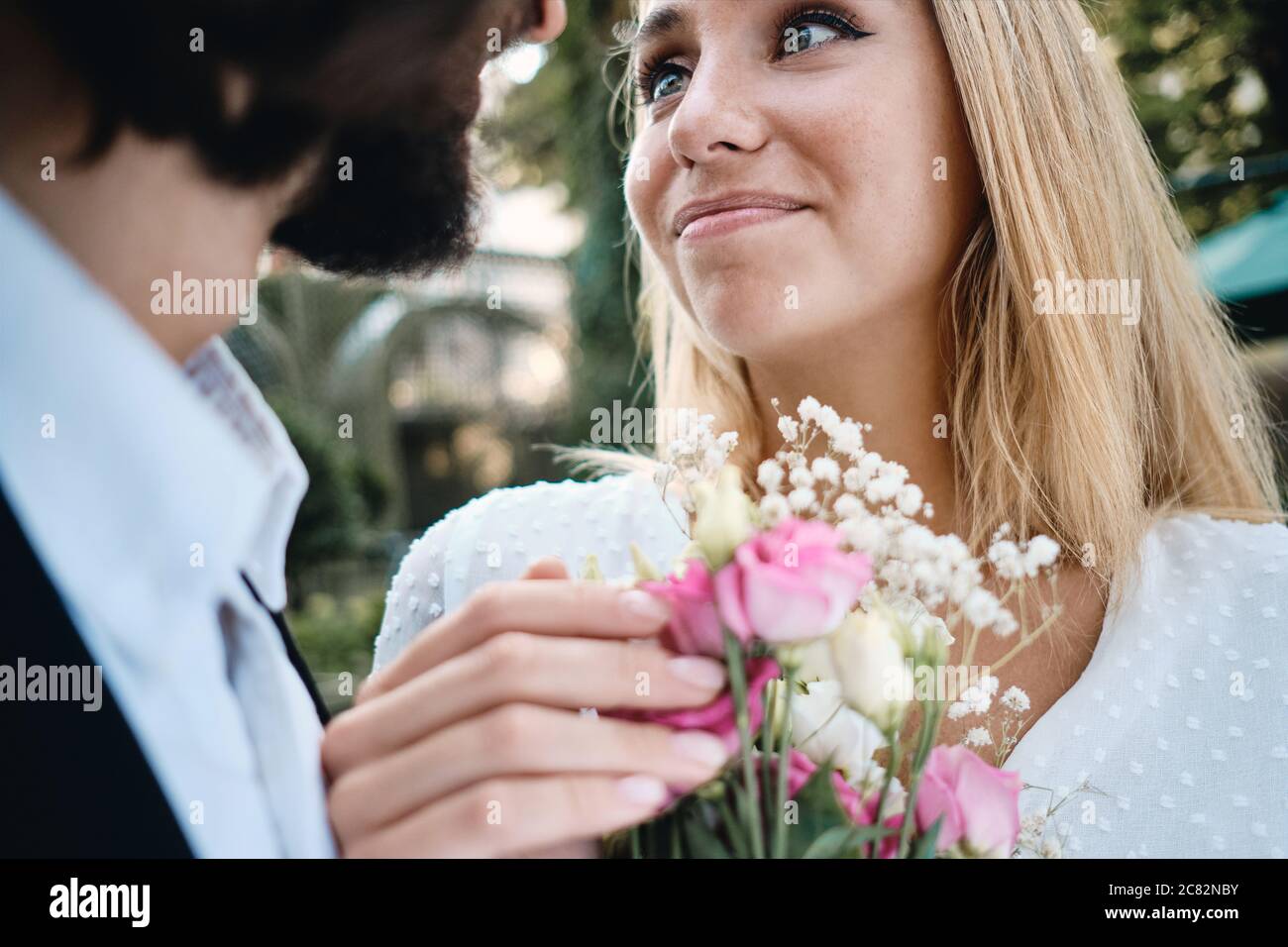Close up beautiful bride with bouquet of flowers dreamily looking at groom outdoor Stock Photo