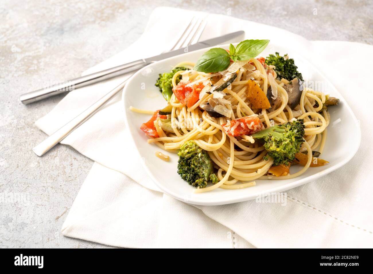 Vegetarian spaghetti with broccoli, tomatoes, bell pepper and eggplant, healthy Mediterranean pasta meal on a white plate and a light rustic backgroun Stock Photo