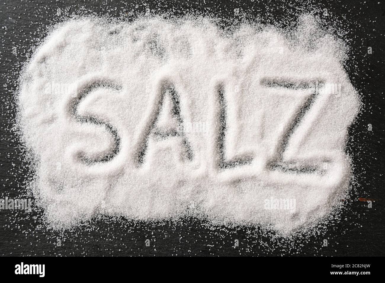 German word SALZ, meaning salt, written in spilled out salt crystals on a dark slate, high angle view from above, selected focus Stock Photo