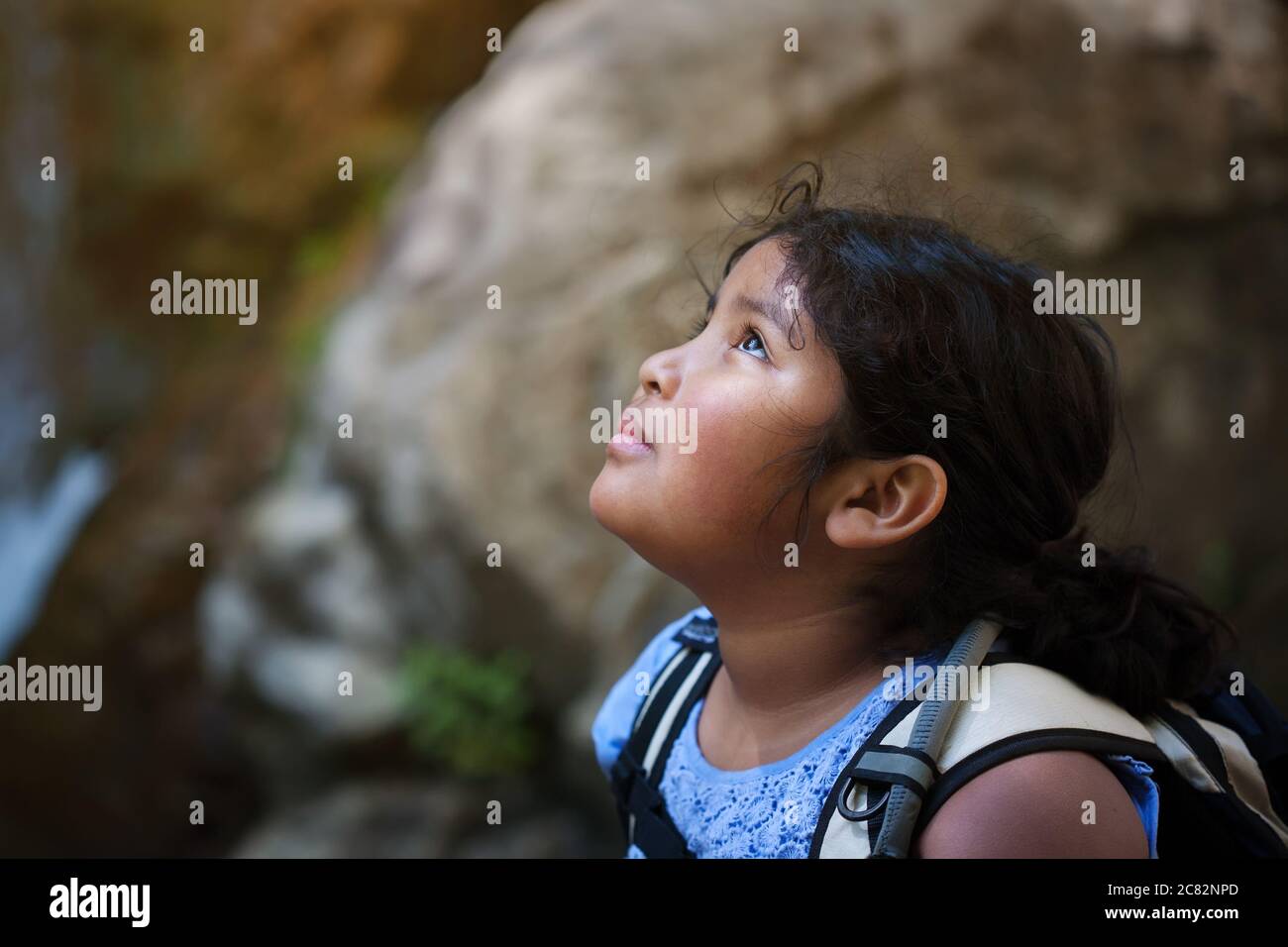 Young girl with hiking backpack looks up towards a difficult hiking trail ahead of her. Stock Photo