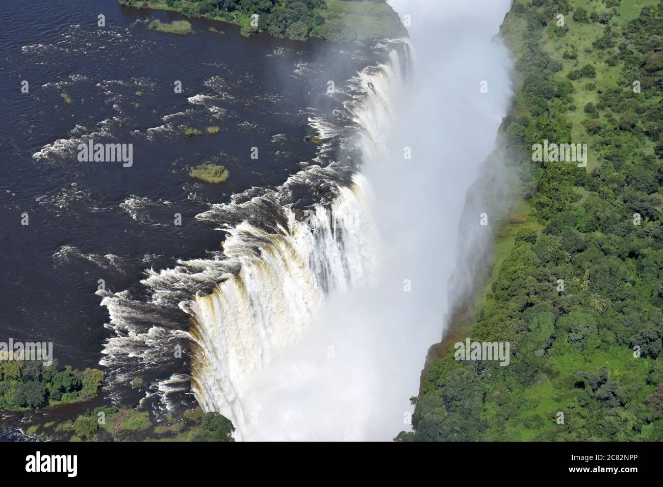 An aerial view of the Zambezi River flowing over the edge of Victoria Falls into the first gorge and into the smoke that thunders. Zimbabwe & Zambia. Stock Photo