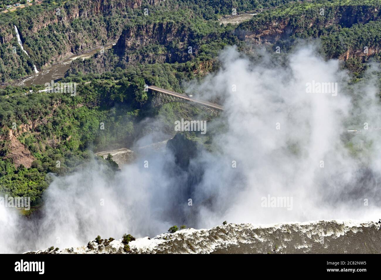 An aerial view of The Smoke That Thunders. Victoria Falls bridge and the gorges can be seen behind the spray from the waterfall.  Zimbabwe and Zambia. Stock Photo