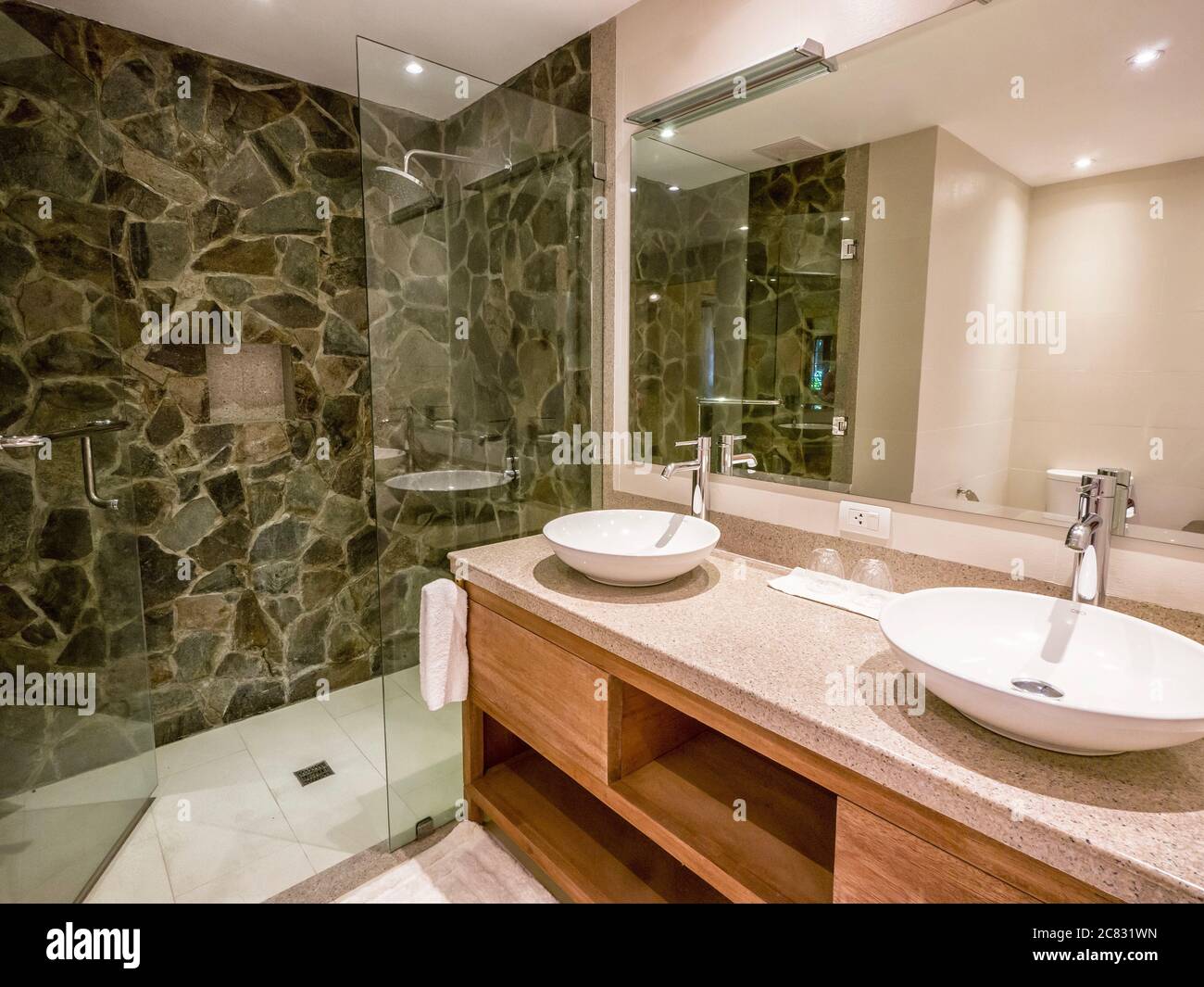 Contemporary bathroom with two round white ceramic vessel sinks on top of granite counter, shower enclosure with natural stone walls. Neutral color. Stock Photo