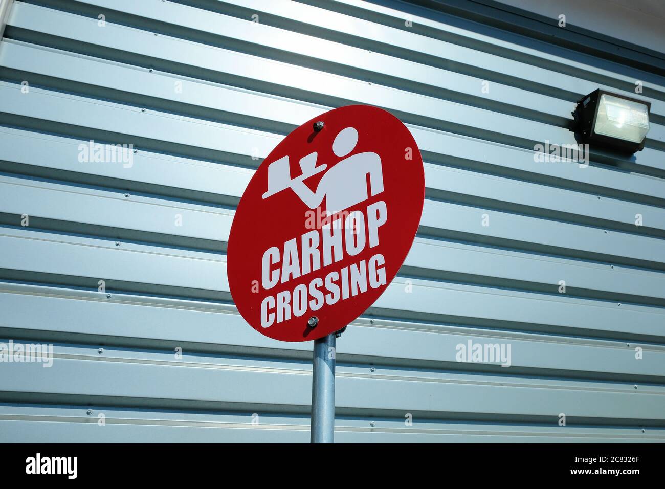 Red carhop crossing sign with icon of a server with a tray, drinks, and food outside a drive thru at a Sonic Drive In fast food restaurant. Stock Photo