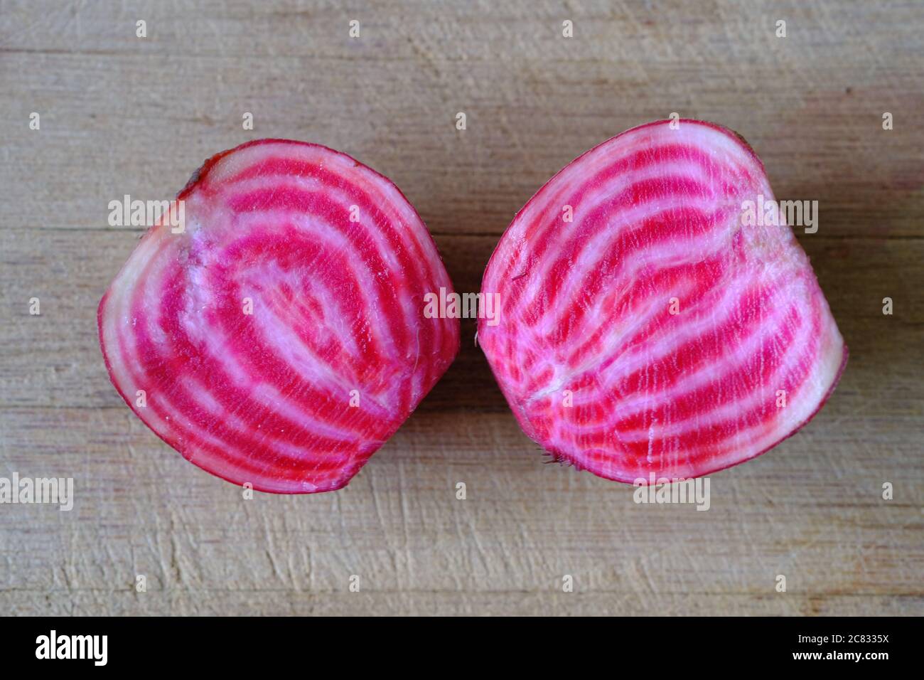 Colourful, cheerful, peppermint rings of red, pink and white hidden inside of a candy cane beet - sliced in two on a wooden chopping board. Stock Photo