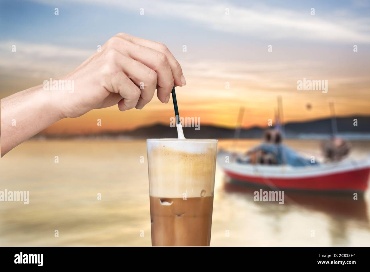 Female hand stirring a straw on a greek cold coffee, freddo cappuccino, outdoors Stock Photo
