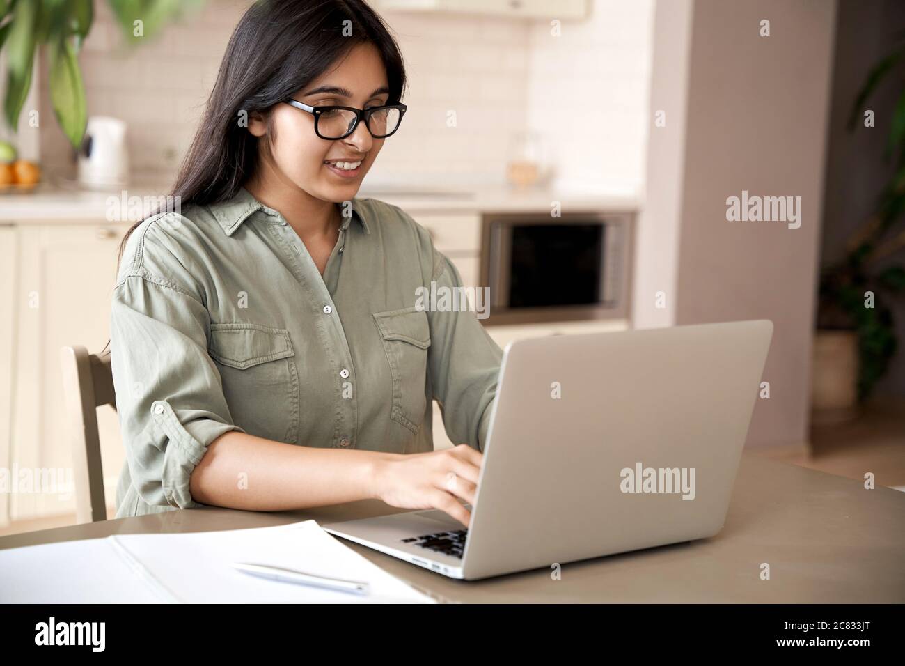 Smiling indian young woman typing on laptop computer working at home office. Stock Photo