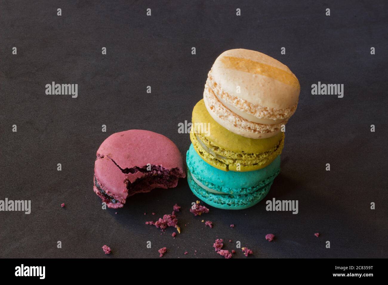 Closeup shot of a stack of colorful macarons and crumbs on a black ...