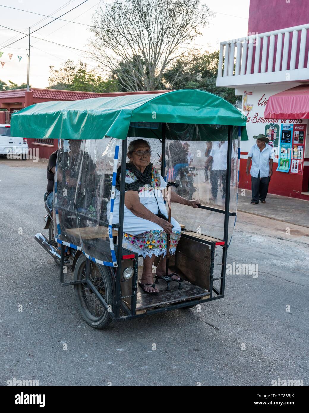 An older Mayan woman in her traditional embroidered huipil rides in a three-wheeled mototaxi in Santa Elena, Yucatan, Mexico. Stock Photo