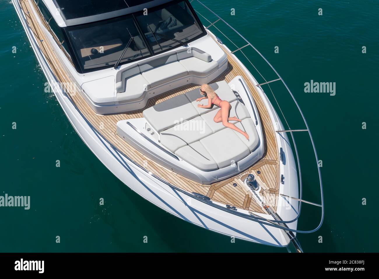 A young woman (18 - 30) in a bikini reclined on the foredeck of a 20M motor yacht. Stock Photo