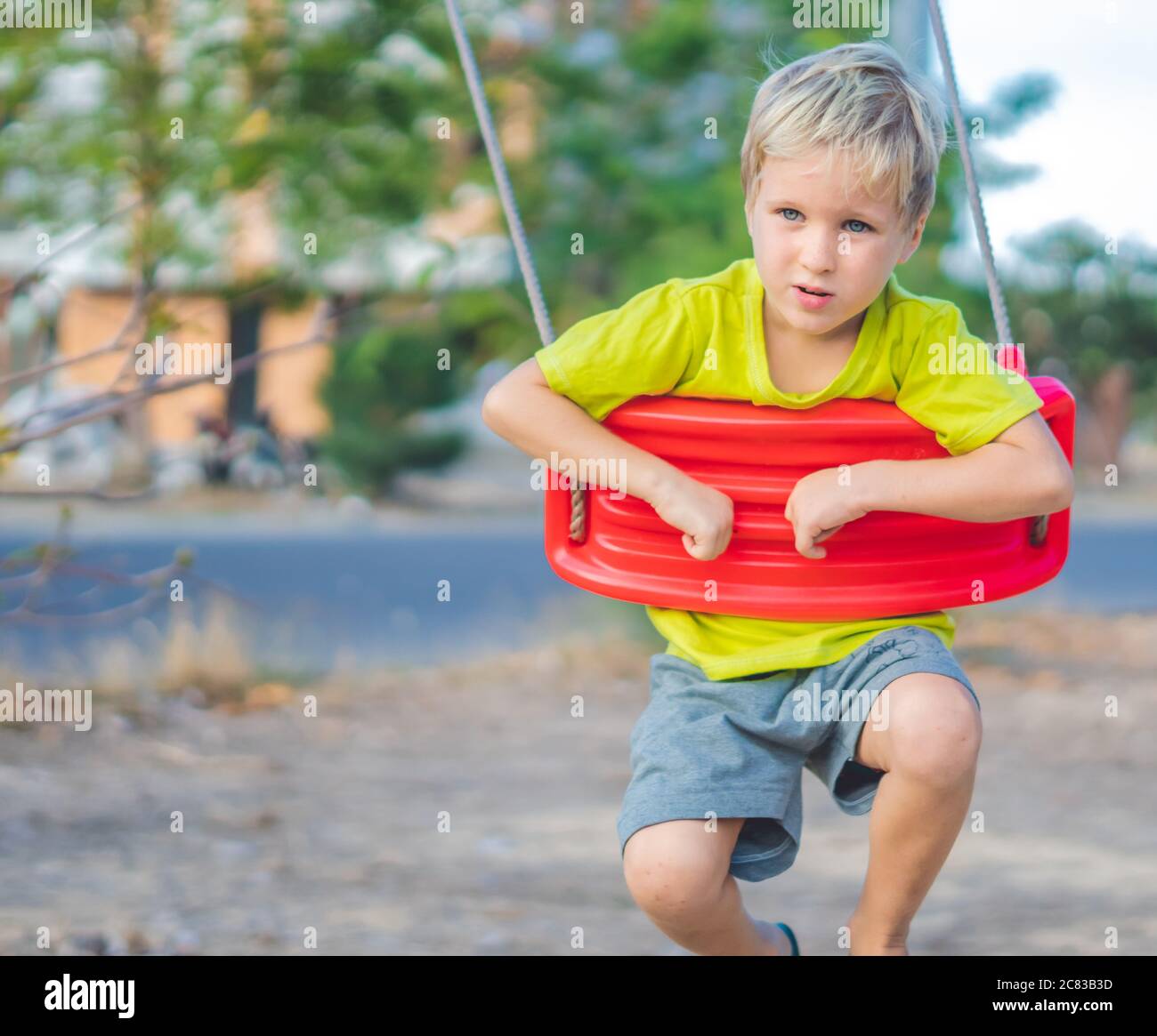 Sad lonely boy sitting on swing, waiting for friends or while parents are busy. Summer, childhood, leisure, friendship and people concept Stock Photo