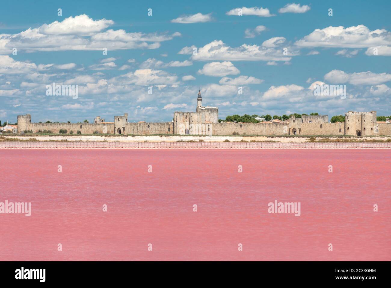 Close up of the vast pink expanse of saltworks in front of the fortified walls of Aigues Mortes, under a blue summer sky with puffy clouds Stock Photo