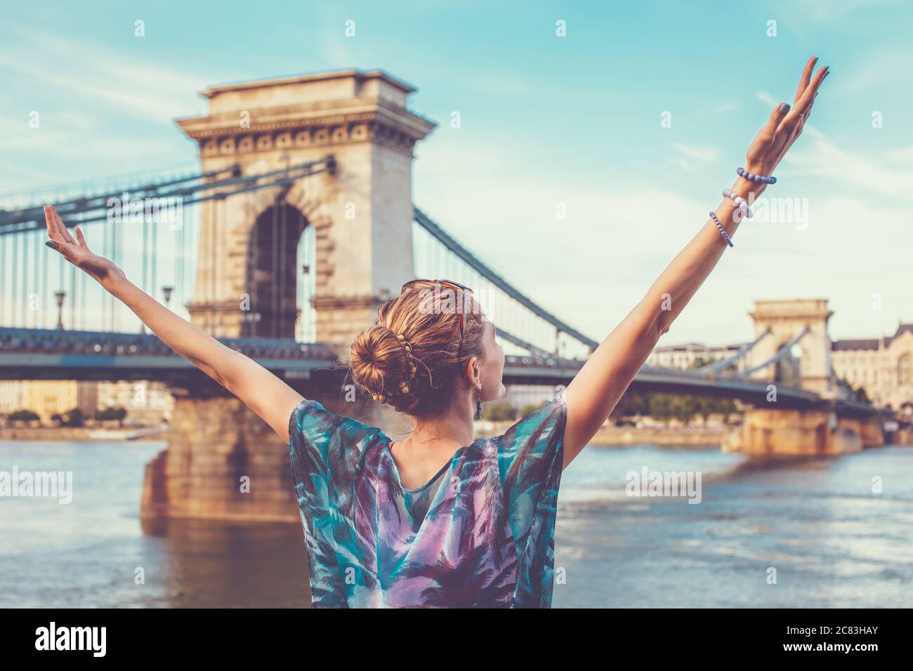 Thankful young redhead woman arms raised at Chain Bridge, Budapest, Hungary Stock Photo