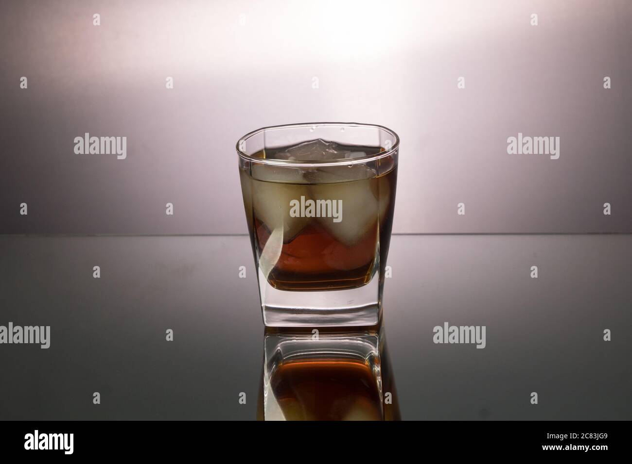 Glass of whiskey with pieces of ice on mirroring table. Horizontal image with copy space. Stock Photo