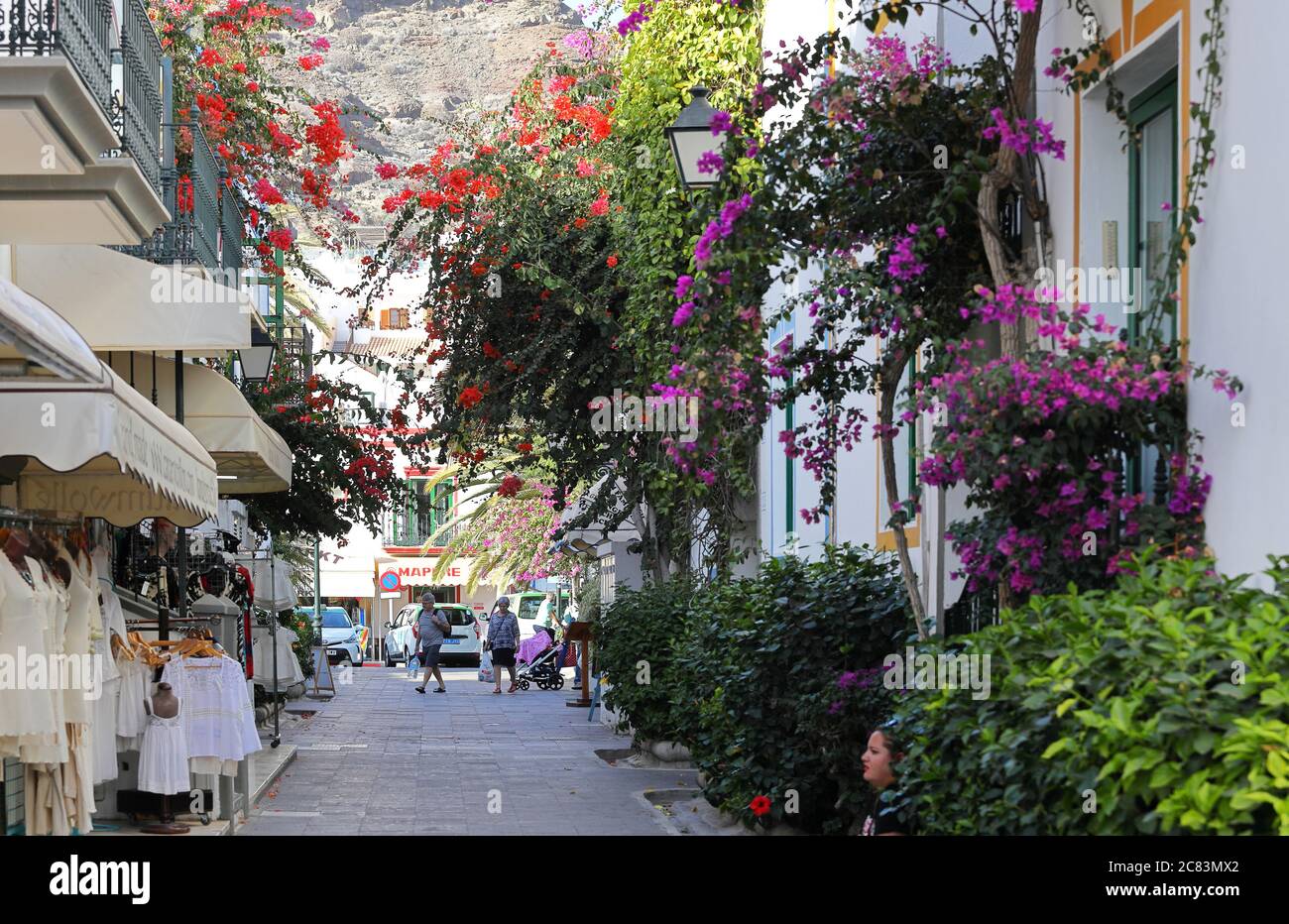 Mogan,Gran Canaria,02.06.2019.Typical street with multi-coloured bougainvillea plants and shops in the Harbour of Mogan Stock Photo