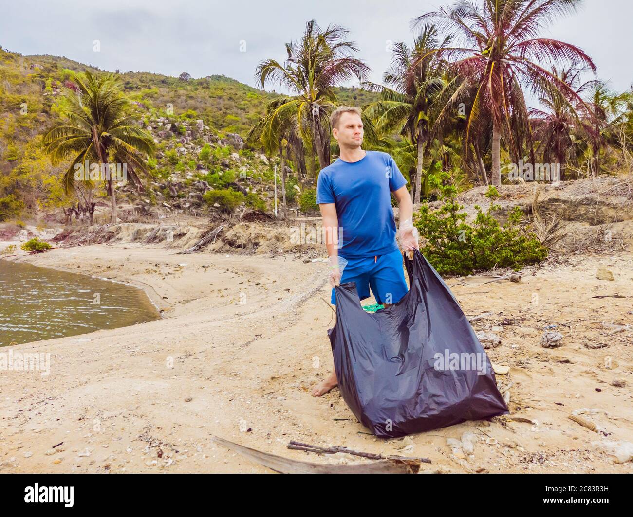 Man in gloves pick up plastic bags that pollute sea. Problem of spilled