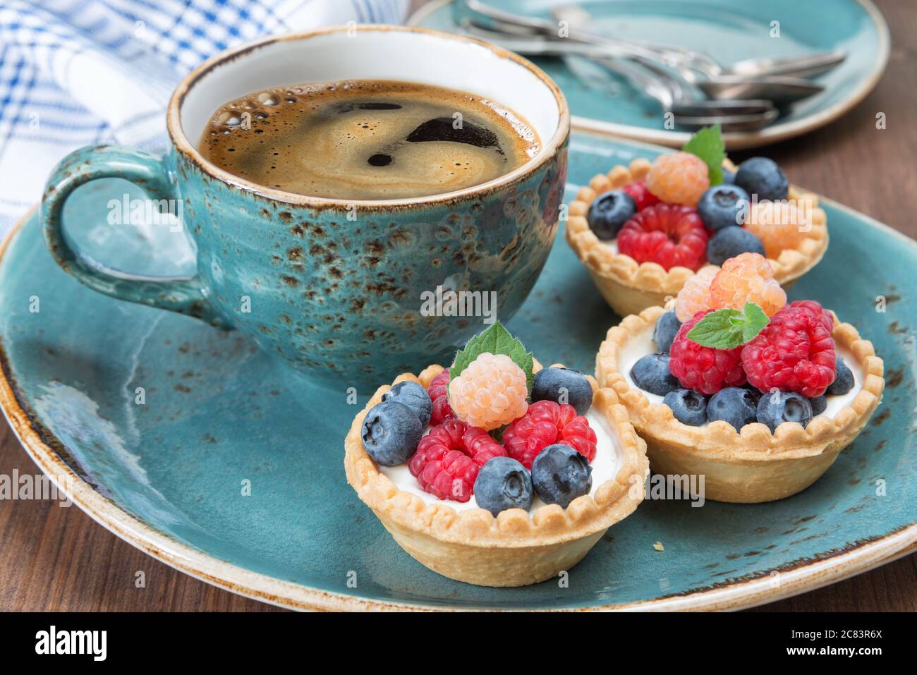 Black coffee in a blue vintage cup and fruit tartlets with raspberries and blueberries Stock Photo